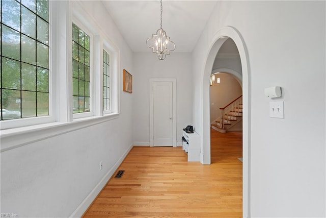 hallway with a notable chandelier, light wood-type flooring, and plenty of natural light