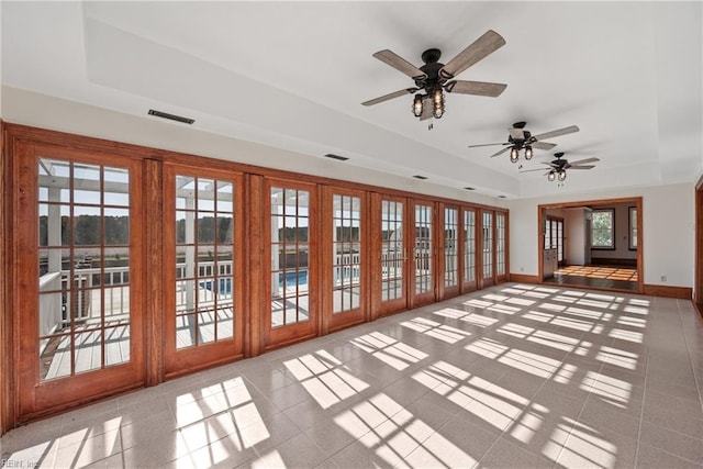 unfurnished living room featuring light tile patterned flooring, ceiling fan, plenty of natural light, and a raised ceiling