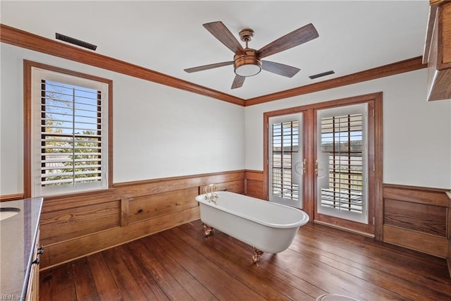 interior space with hardwood / wood-style floors, wood walls, a bathing tub, ceiling fan, and crown molding