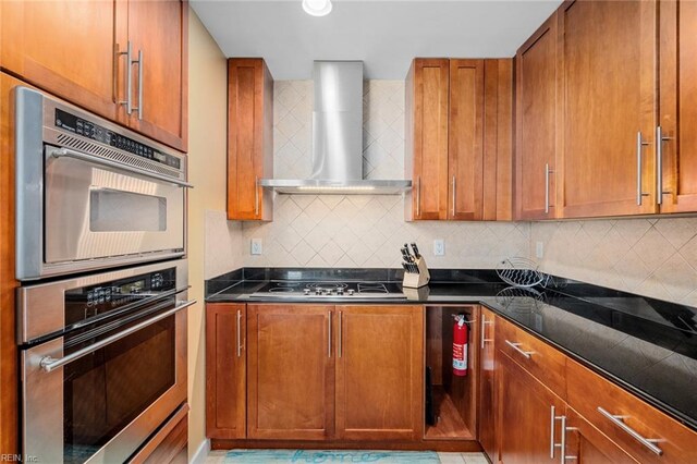 kitchen with stainless steel double oven, decorative backsplash, wall chimney range hood, and gas cooktop