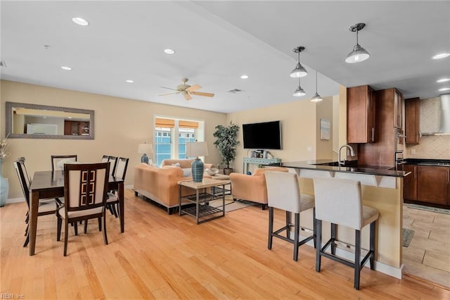 kitchen featuring decorative backsplash, wall chimney exhaust hood, pendant lighting, light wood-type flooring, and ceiling fan