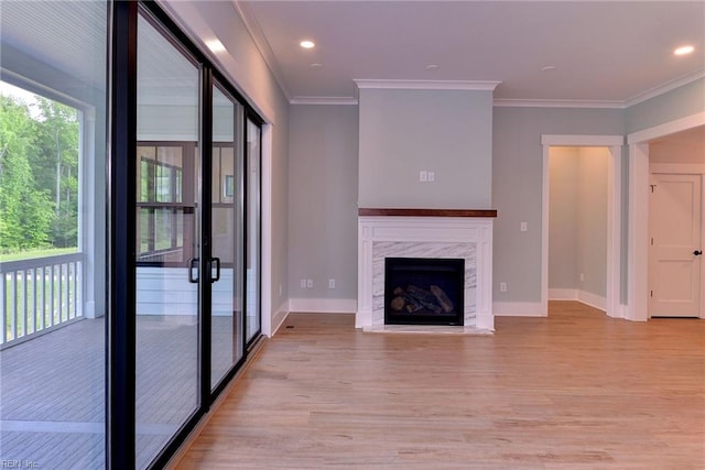 unfurnished living room featuring crown molding, a wealth of natural light, light wood-type flooring, and a high end fireplace