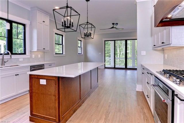 kitchen featuring ventilation hood, a sink, light wood finished floors, stainless steel appliances, and ornamental molding