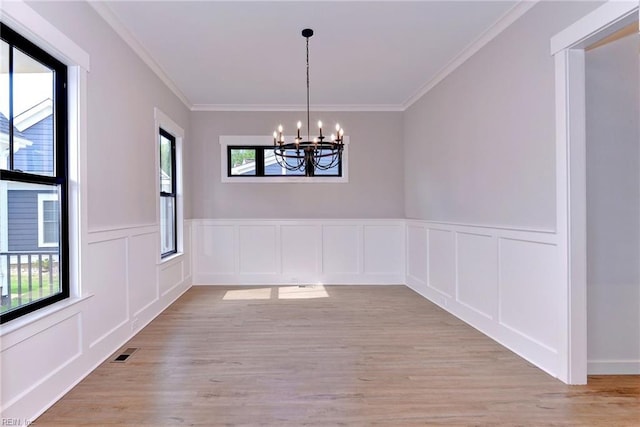 unfurnished dining area with light wood-type flooring, crown molding, an inviting chandelier, and plenty of natural light