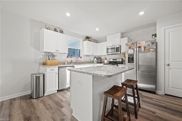 kitchen featuring a breakfast bar area, appliances with stainless steel finishes, a kitchen island, white cabinetry, and light hardwood / wood-style flooring