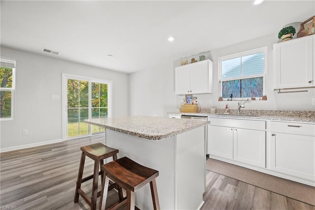 kitchen with white cabinets, a kitchen island, a kitchen breakfast bar, light hardwood / wood-style flooring, and sink