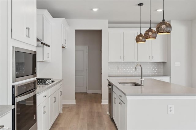 kitchen featuring appliances with stainless steel finishes, light wood-type flooring, hanging light fixtures, white cabinetry, and a center island with sink