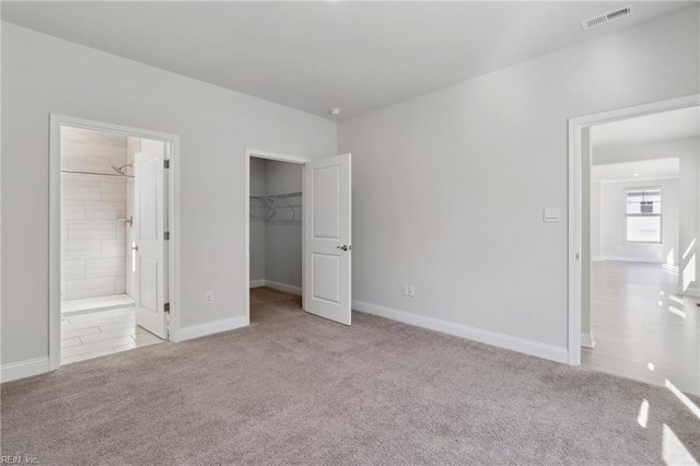 unfurnished bedroom with ensuite bathroom, a walk in closet, a closet, and light colored carpet