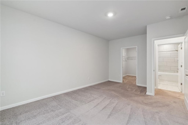 unfurnished bedroom featuring a closet, a spacious closet, light colored carpet, and ensuite bathroom