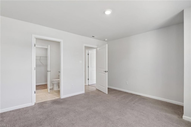 unfurnished bedroom with a closet, light carpet, ensuite bathroom, and a walk in closet