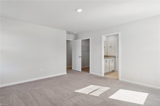 unfurnished bedroom with a spacious closet, light colored carpet, a closet, and ensuite bath