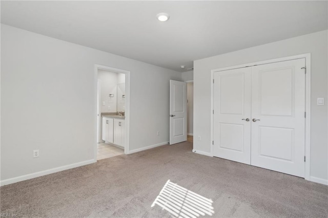 unfurnished bedroom with a closet, ensuite bath, light colored carpet, and sink