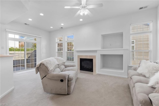 carpeted living room with a tiled fireplace and ceiling fan