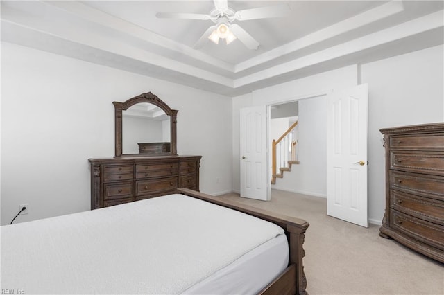 bedroom with light colored carpet, a tray ceiling, and ceiling fan