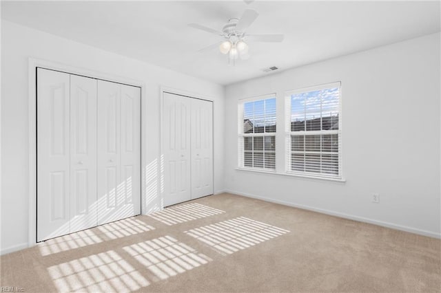 unfurnished bedroom featuring light carpet, two closets, and ceiling fan