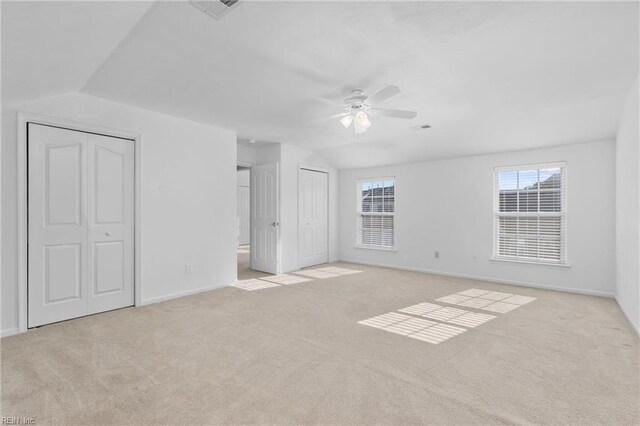 unfurnished bedroom with lofted ceiling, light carpet, multiple closets, and ceiling fan