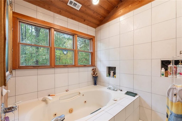 bathroom featuring tile walls, tiled bath, plenty of natural light, and vaulted ceiling