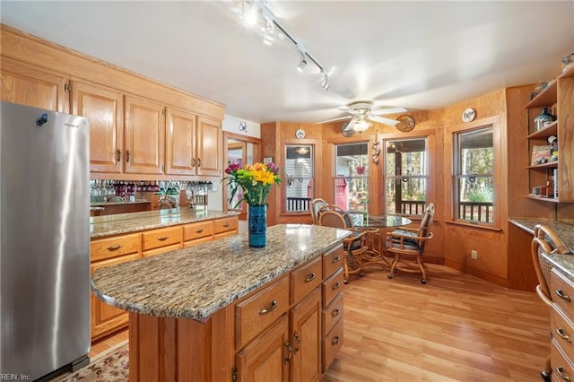 kitchen with light wood-type flooring, light stone counters, a center island, and stainless steel refrigerator