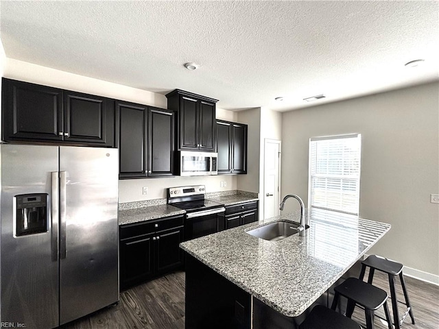 kitchen with a kitchen island with sink, stainless steel appliances, sink, and dark hardwood / wood-style flooring