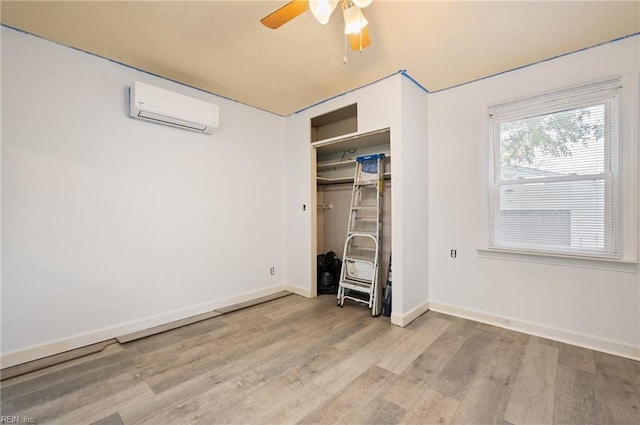 unfurnished bedroom featuring a wall mounted AC, light hardwood / wood-style flooring, a closet, and ceiling fan