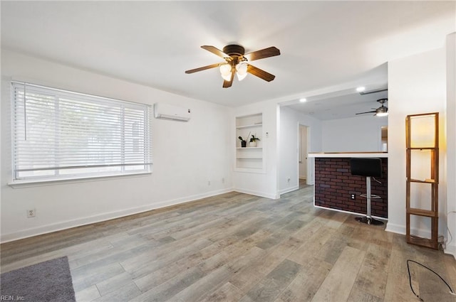 unfurnished living room featuring built in features, a wall mounted air conditioner, light hardwood / wood-style floors, and ceiling fan