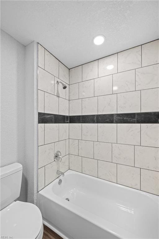 bathroom with toilet, tiled shower / bath combo, and a textured ceiling