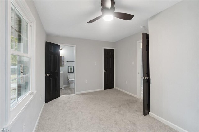 unfurnished bedroom featuring light colored carpet, ceiling fan, and ensuite bath