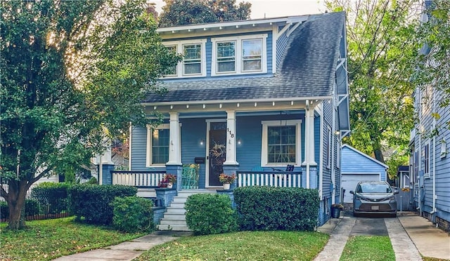 view of front of home featuring an outbuilding, covered porch, a front yard, and a garage