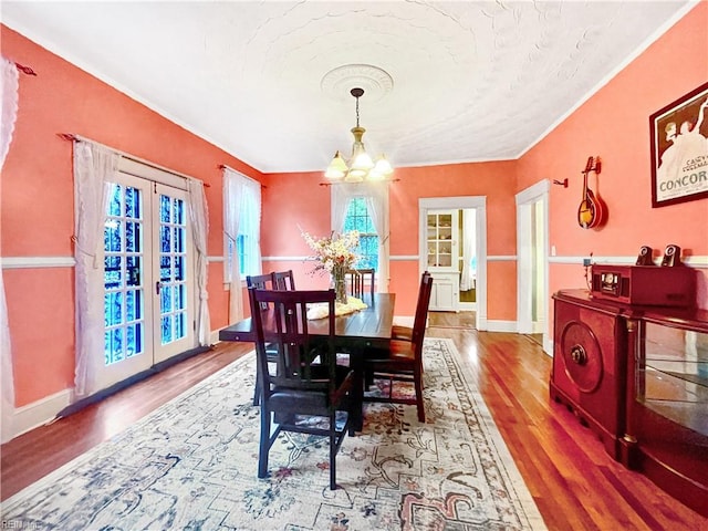 dining space with french doors, ornamental molding, a notable chandelier, and hardwood / wood-style flooring