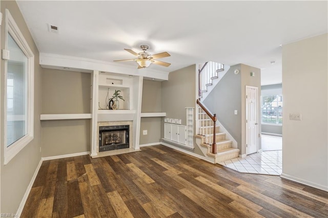 unfurnished living room featuring built in shelves, hardwood / wood-style flooring, and ceiling fan