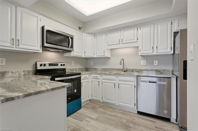 kitchen with stainless steel appliances, sink, white cabinets, light stone counters, and light hardwood / wood-style floors