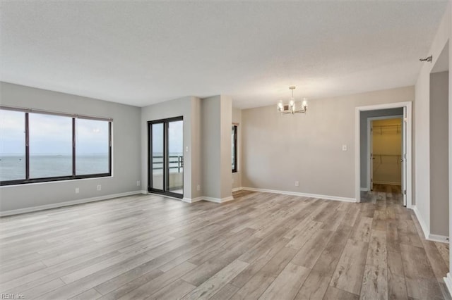 spare room with a chandelier, light hardwood / wood-style flooring, and a water view