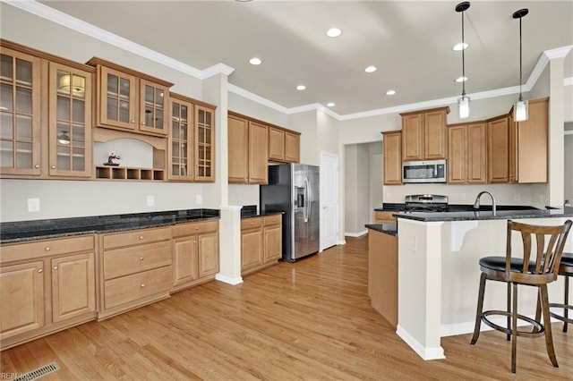 kitchen featuring crown molding, dark stone counters, appliances with stainless steel finishes, hanging light fixtures, and light hardwood / wood-style floors