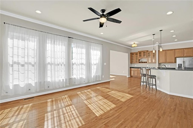 unfurnished living room featuring ceiling fan, sink, light hardwood / wood-style floors, and crown molding