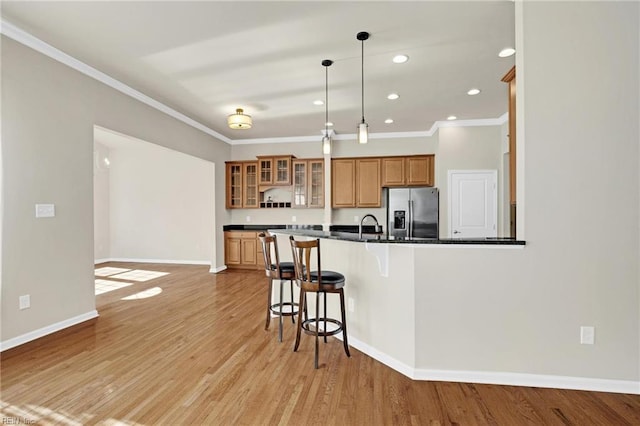 kitchen with pendant lighting, light wood-type flooring, kitchen peninsula, and stainless steel fridge