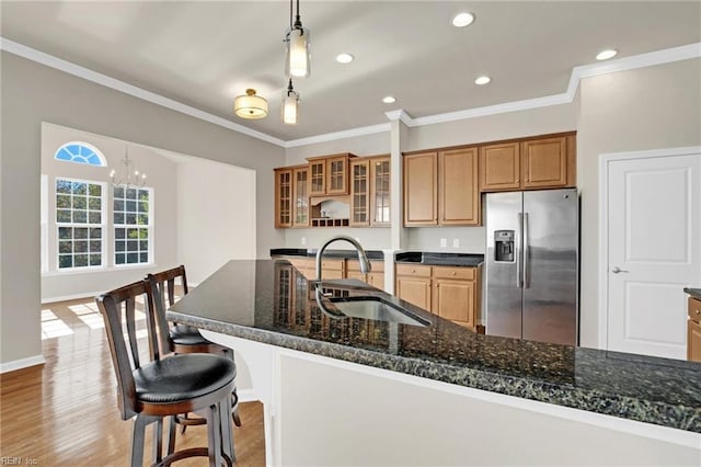 kitchen featuring dark stone counters, stainless steel refrigerator with ice dispenser, hanging light fixtures, sink, and light wood-type flooring