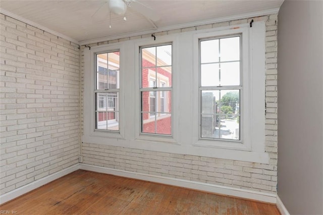 unfurnished room featuring brick wall, ornamental molding, wood-type flooring, and ceiling fan