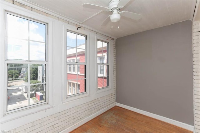 empty room with brick wall, wood-type flooring, and ceiling fan