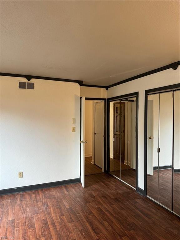 unfurnished bedroom featuring multiple closets, crown molding, and dark hardwood / wood-style floors