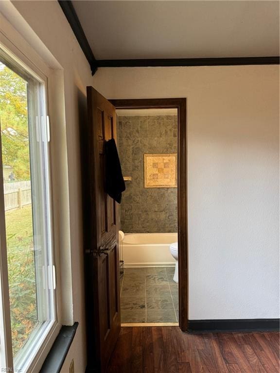 interior space with a bath, toilet, ornamental molding, and hardwood / wood-style floors