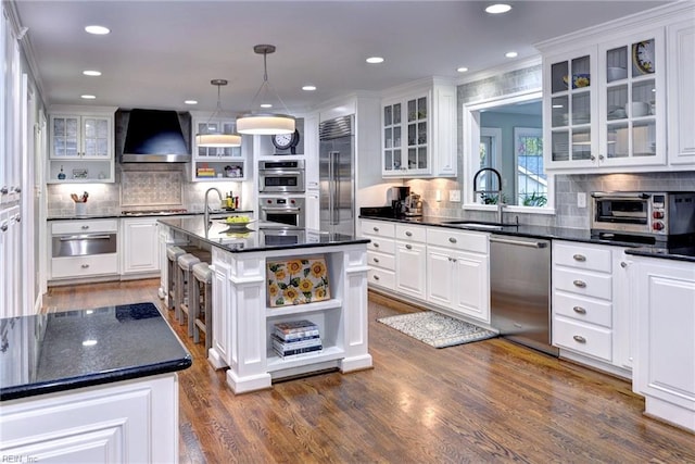 kitchen with an island with sink, wall chimney exhaust hood, white cabinetry, and stainless steel appliances