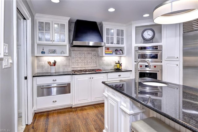 kitchen featuring stainless steel appliances, white cabinetry, dark stone counters, dark hardwood / wood-style floors, and wall chimney range hood