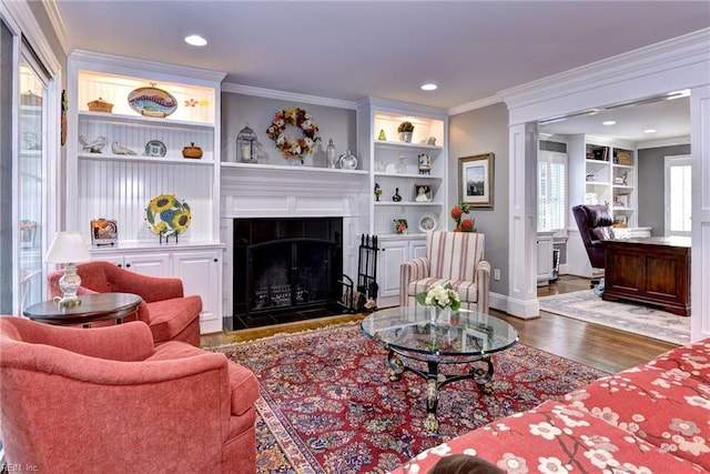 living room with dark hardwood / wood-style flooring, built in features, a tile fireplace, and ornamental molding