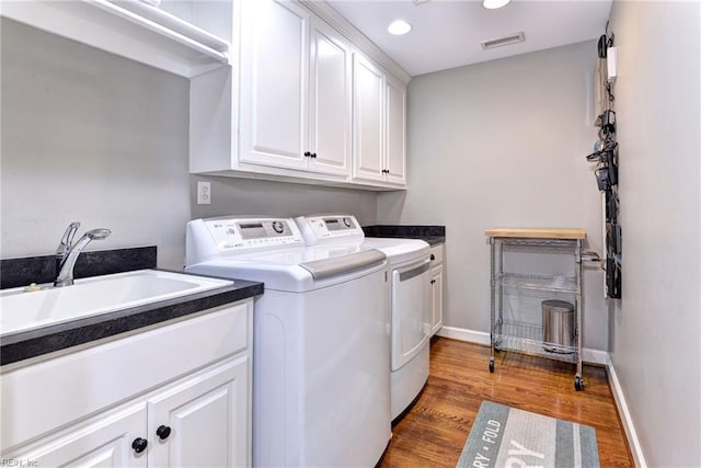 clothes washing area with cabinets, hardwood / wood-style flooring, separate washer and dryer, and sink