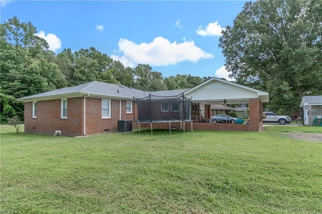 rear view of property with central AC, a lawn, and a trampoline