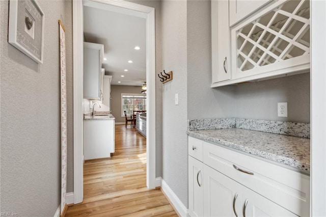 bar featuring white cabinetry, light wood-type flooring, sink, and light stone counters