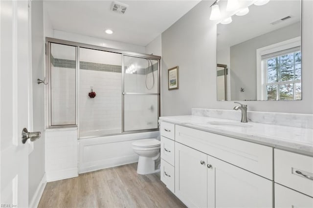 full bathroom featuring hardwood / wood-style floors, vanity, toilet, and enclosed tub / shower combo