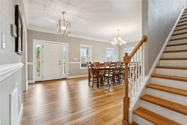 entrance foyer with ornamental molding, light wood-type flooring, and an inviting chandelier