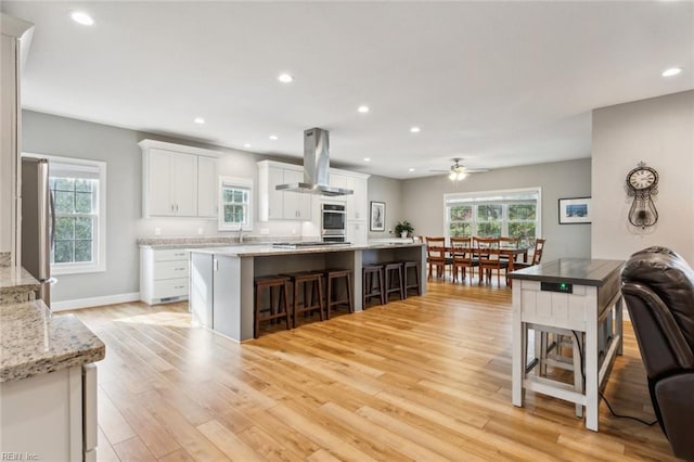 kitchen featuring appliances with stainless steel finishes, light hardwood / wood-style floors, white cabinets, wall chimney exhaust hood, and a center island