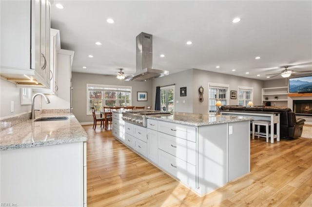 kitchen featuring island exhaust hood, white cabinetry, a large island, light stone countertops, and light hardwood / wood-style flooring